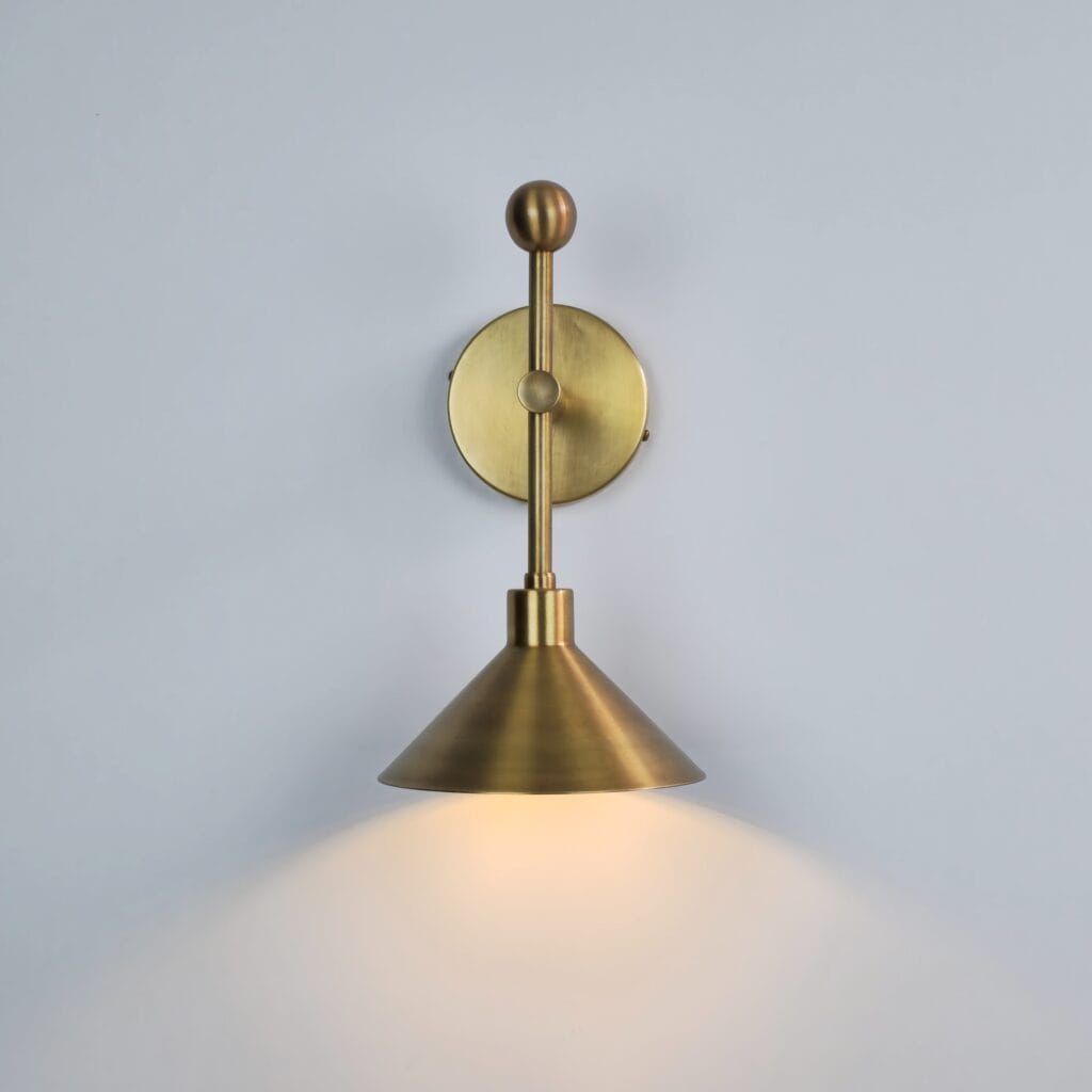 Mid-century modern brass wall lamp with a brushed metallic conical shade, a vertical straight rod with sphere accents, and a circular wall mount casting a bright down-focused glow.