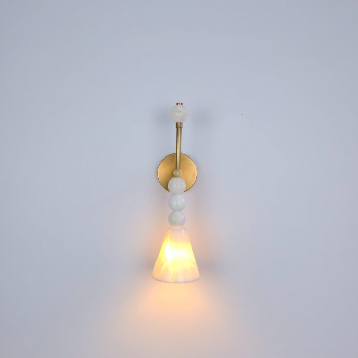 Modern Alabaster wall Light with a conical translucent alabaster glass shade glowing warmly against a wall.
