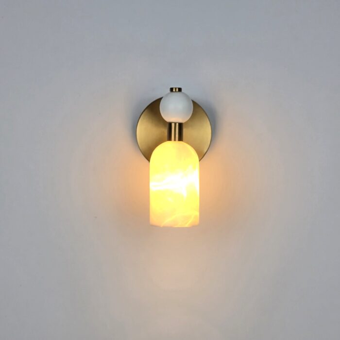 Handmade Alabaster Stone Sconce, featuring a premium brass finish and genuine alabaster stone. The design highlights a circular metallic backplate with a curved alabaster shade that casts a warm downward glow. This minimalist artisan sconce adds organic texture and luxury to modern interior wall decor.