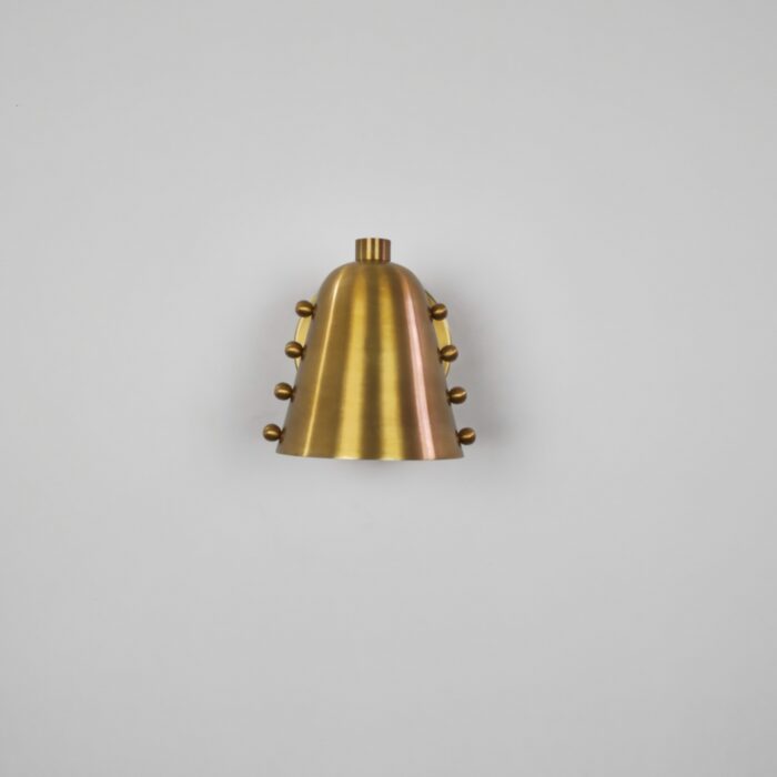 Mid-Century Modern Wall Sconce in antique brass finish with decorative side studs emitting warm downlight